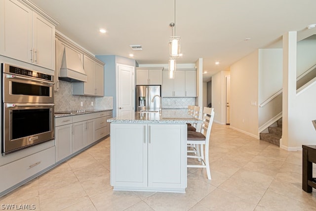 kitchen featuring gray cabinetry, appliances with stainless steel finishes, premium range hood, tasteful backsplash, and pendant lighting