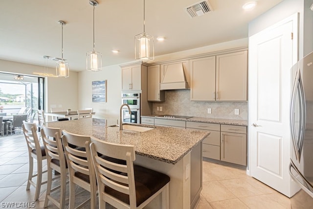 kitchen with light tile floors, a kitchen bar, appliances with stainless steel finishes, hanging light fixtures, and custom range hood