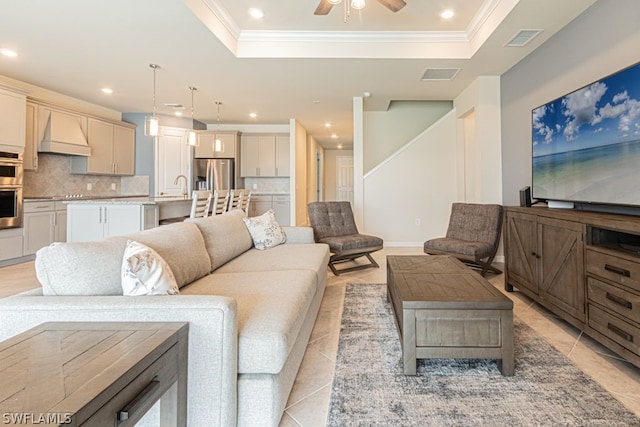 tiled living room with ceiling fan, crown molding, a raised ceiling, and sink