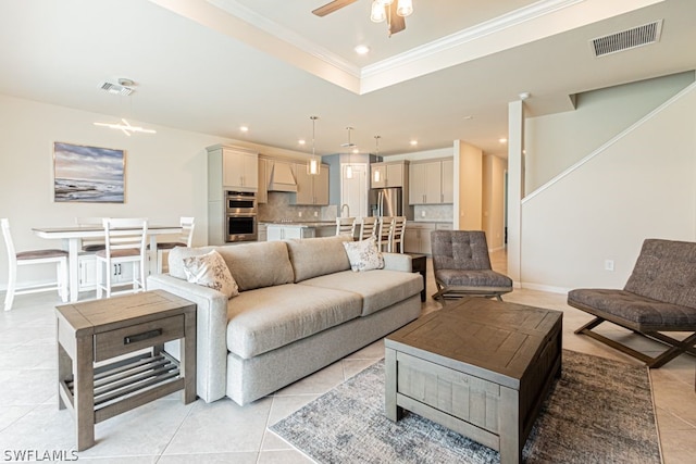 tiled living room with crown molding, ceiling fan, a tray ceiling, and sink