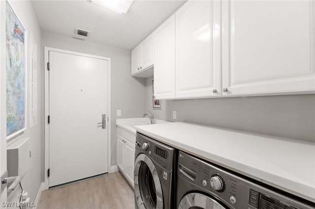 clothes washing area with cabinets, washing machine and dryer, sink, and light hardwood / wood-style flooring