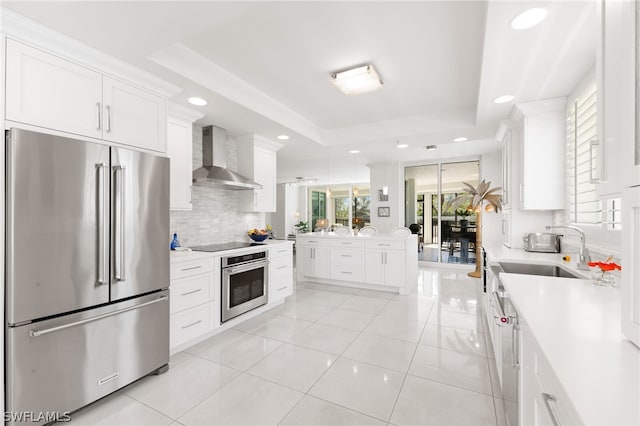 kitchen with stainless steel appliances, white cabinetry, tasteful backsplash, wall chimney exhaust hood, and a tray ceiling