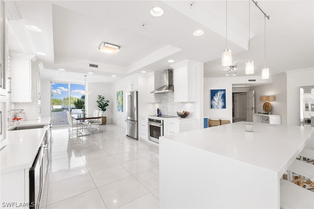 kitchen with stainless steel appliances, a kitchen island, pendant lighting, white cabinets, and wall chimney exhaust hood