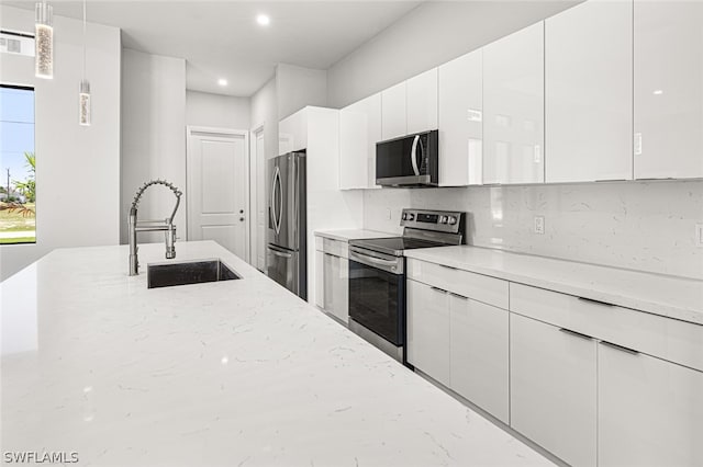 kitchen with decorative light fixtures, appliances with stainless steel finishes, white cabinets, backsplash, and sink