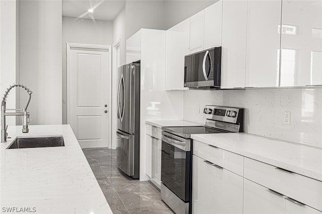 kitchen featuring light stone countertops, appliances with stainless steel finishes, white cabinets, dark tile floors, and sink