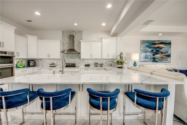 kitchen featuring white cabinets, tasteful backsplash, light stone counters, and wall chimney range hood