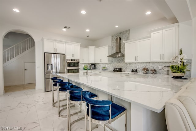 kitchen featuring white cabinetry, a breakfast bar, stainless steel appliances, tasteful backsplash, and wall chimney exhaust hood