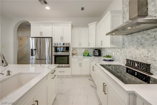 kitchen with backsplash, light stone counters, appliances with stainless steel finishes, and wall chimney range hood