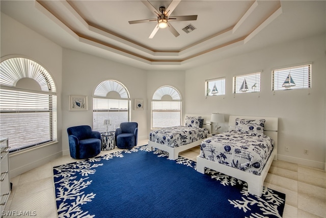 bedroom with light tile floors, a tray ceiling, and ceiling fan