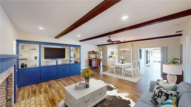 living room featuring ceiling fan with notable chandelier, beam ceiling, a fireplace, and light hardwood / wood-style flooring