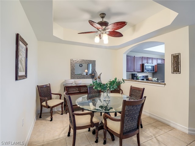 dining space featuring a raised ceiling, ceiling fan, and light tile patterned floors