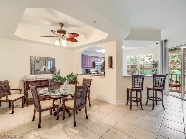 tiled dining area with ceiling fan and a tray ceiling