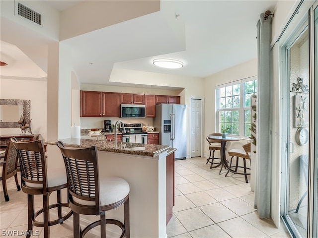 kitchen featuring kitchen peninsula, appliances with stainless steel finishes, a kitchen bar, sink, and light tile patterned floors