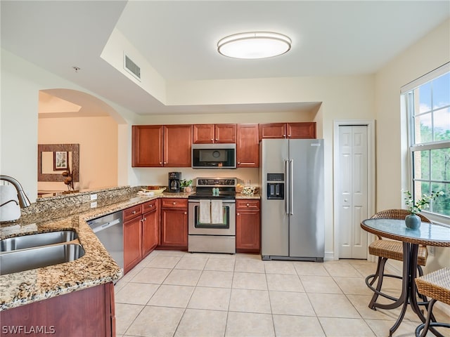 kitchen with kitchen peninsula, light stone counters, stainless steel appliances, sink, and light tile patterned flooring