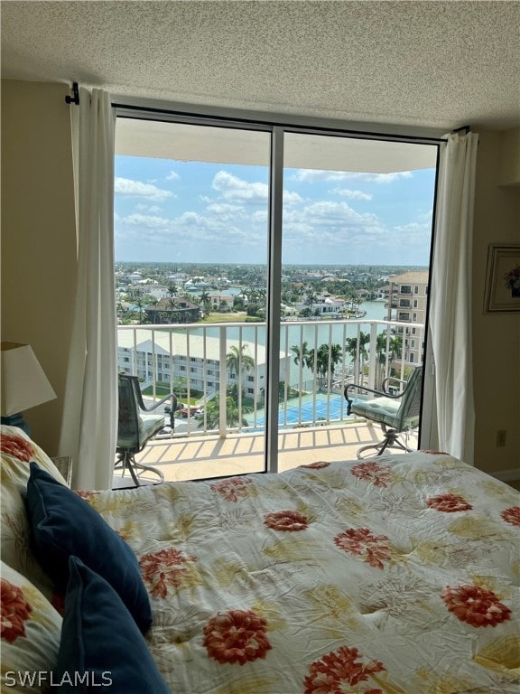 bedroom featuring a water view, access to outside, expansive windows, and a textured ceiling