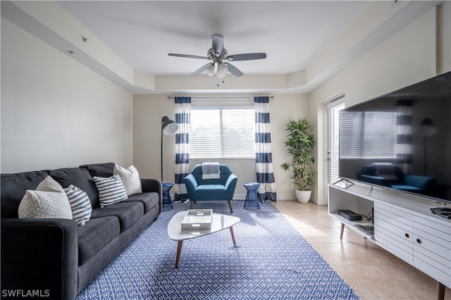 living room with a raised ceiling, ceiling fan, and light tile floors