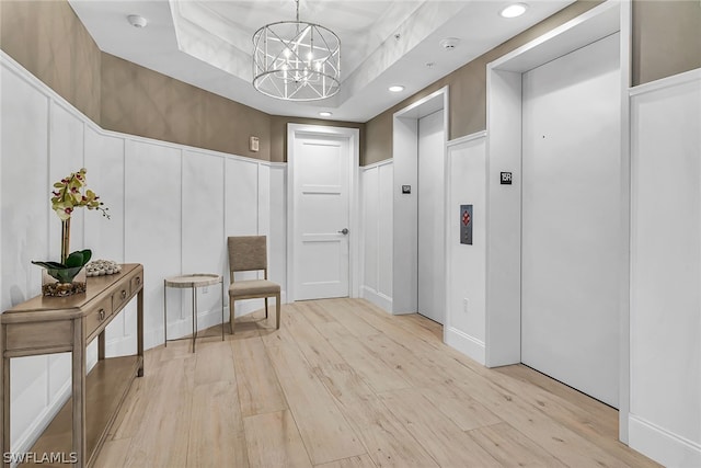 living area with light hardwood / wood-style floors, elevator, a chandelier, and a tray ceiling