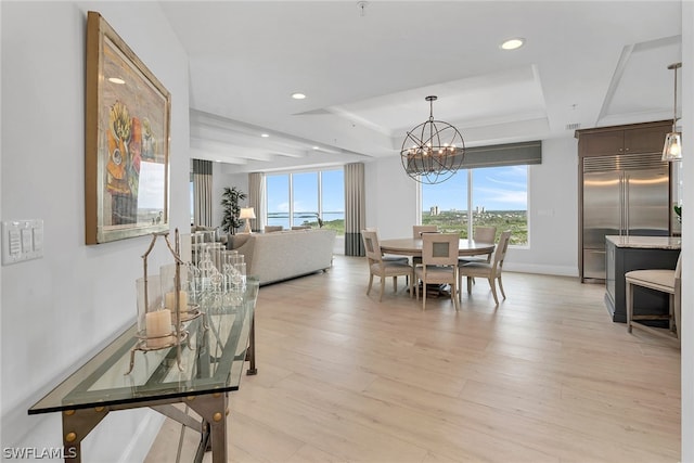 dining space with a raised ceiling, light wood-type flooring, and an inviting chandelier