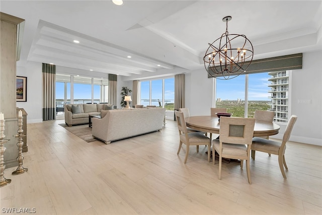 dining space with a notable chandelier, a tray ceiling, and light wood-type flooring