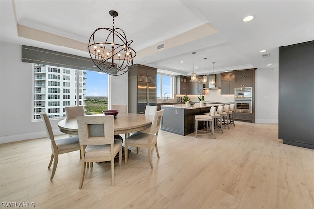 dining room featuring light hardwood / wood-style flooring, a tray ceiling, a notable chandelier, and sink