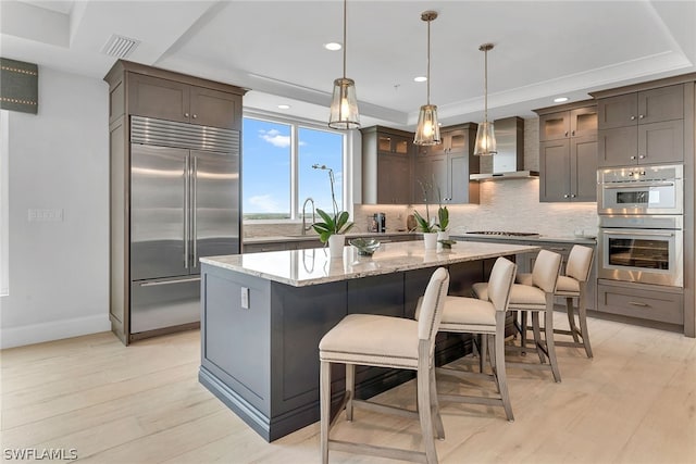 kitchen with wall chimney range hood, a kitchen island, tasteful backsplash, and appliances with stainless steel finishes