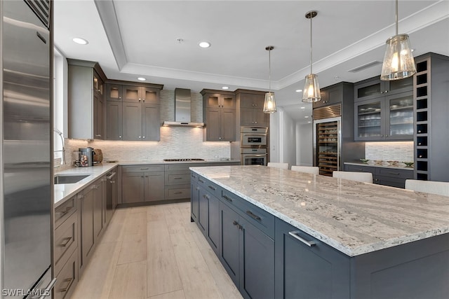 kitchen with stainless steel appliances, wall chimney range hood, gray cabinets, backsplash, and hanging light fixtures