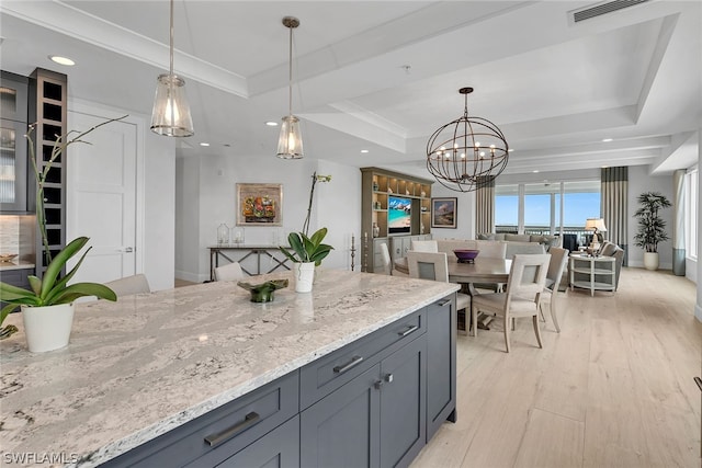 kitchen featuring a tray ceiling, light stone countertops, light hardwood / wood-style flooring, and an inviting chandelier