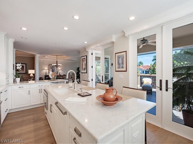 kitchen with french doors, light wood-style flooring, a kitchen island with sink, a sink, and white cabinetry