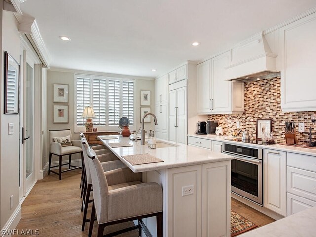 kitchen with a kitchen island with sink, sink, oven, a breakfast bar area, and light wood-type flooring