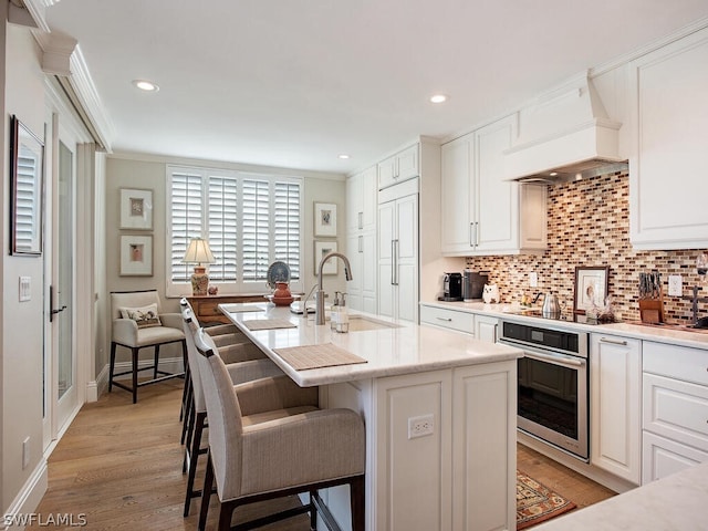 kitchen featuring decorative backsplash, ornamental molding, oven, custom exhaust hood, and a sink