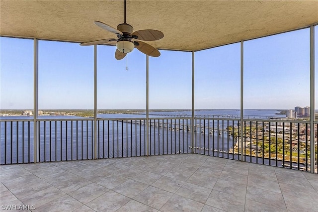 unfurnished sunroom featuring ceiling fan and a water view