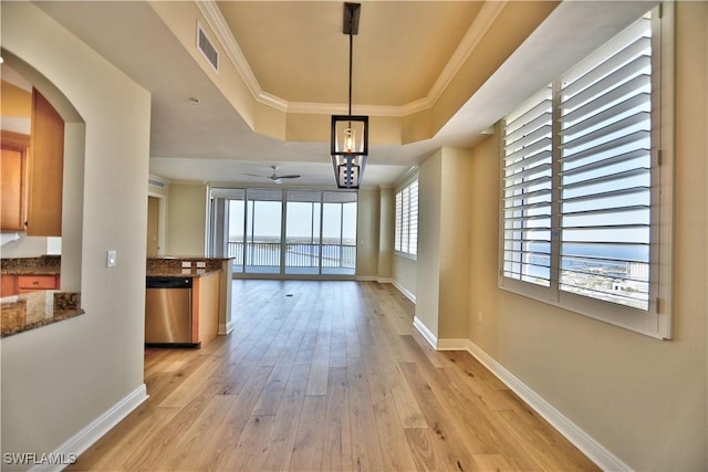 corridor with crown molding, a wealth of natural light, light wood-type flooring, and a tray ceiling