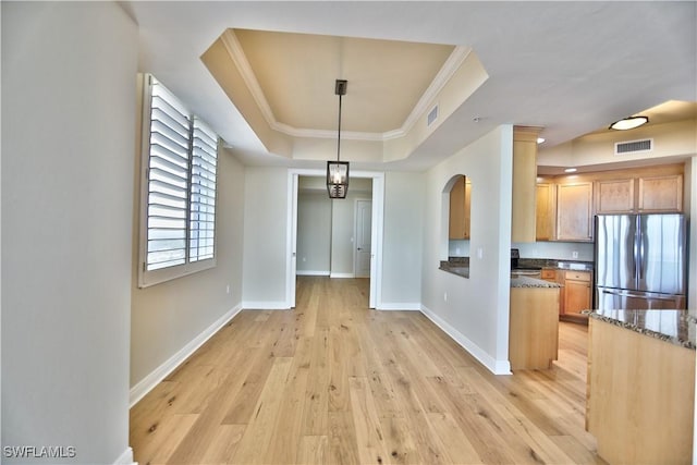 unfurnished dining area featuring ornamental molding, a raised ceiling, and light wood-type flooring