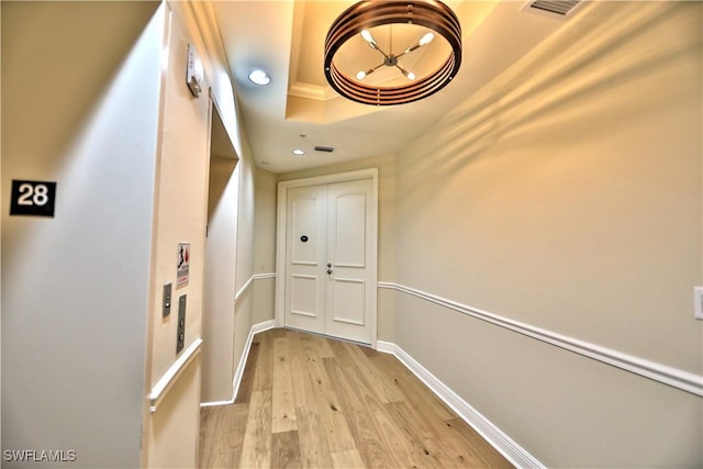 corridor featuring light hardwood / wood-style flooring, ornamental molding, and a raised ceiling