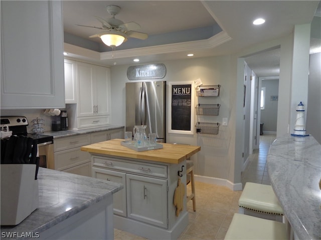 kitchen with electric stove, stainless steel fridge, white cabinets, butcher block counters, and a tray ceiling