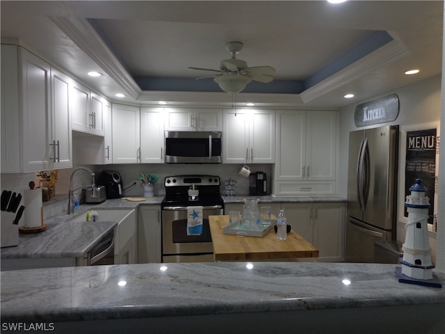 kitchen with stainless steel appliances, ceiling fan, white cabinets, and a tray ceiling