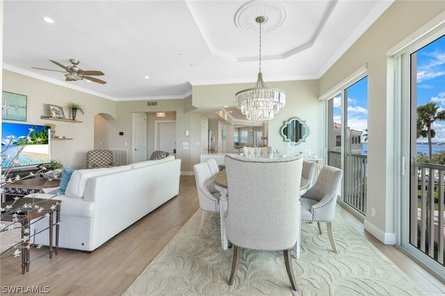 dining space featuring a raised ceiling, ceiling fan with notable chandelier, light hardwood / wood-style flooring, and ornamental molding