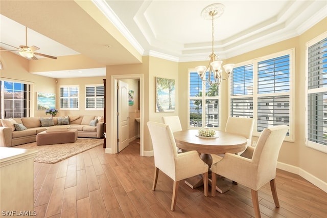 dining room featuring ceiling fan with notable chandelier, ornamental molding, light hardwood / wood-style flooring, and a tray ceiling