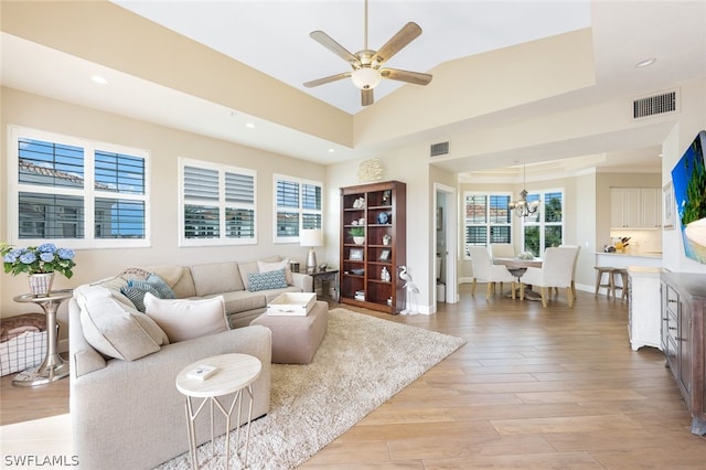 living room with ceiling fan with notable chandelier, light hardwood / wood-style floors, and a tray ceiling