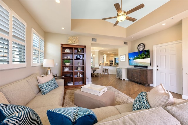 living room with a raised ceiling, ceiling fan, and light hardwood / wood-style flooring