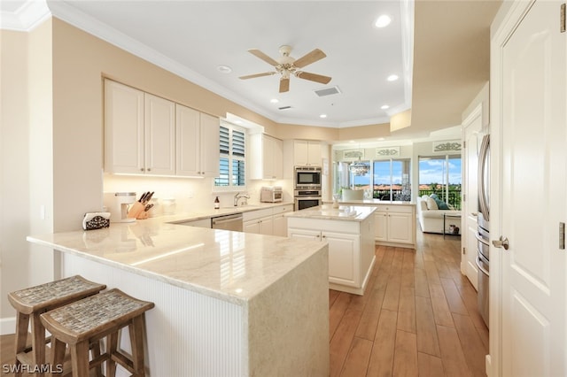 kitchen featuring light hardwood / wood-style flooring, stainless steel dishwasher, kitchen peninsula, a kitchen bar, and white cabinets