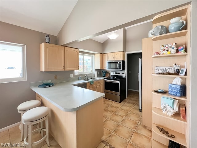 kitchen featuring light brown cabinets, light tile floors, a kitchen bar, appliances with stainless steel finishes, and lofted ceiling