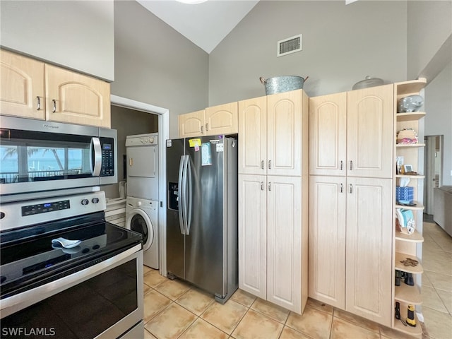 kitchen with stacked washer and dryer, appliances with stainless steel finishes, high vaulted ceiling, light tile floors, and light brown cabinetry