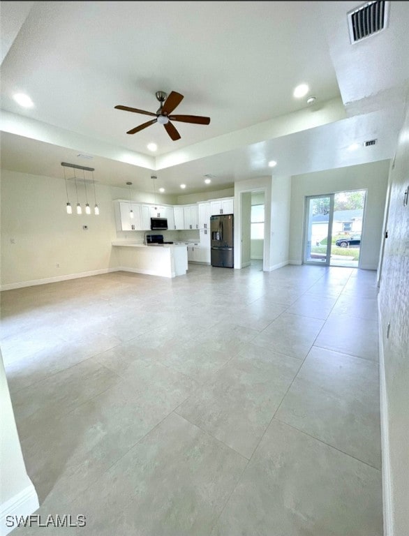 unfurnished living room featuring ceiling fan and a raised ceiling