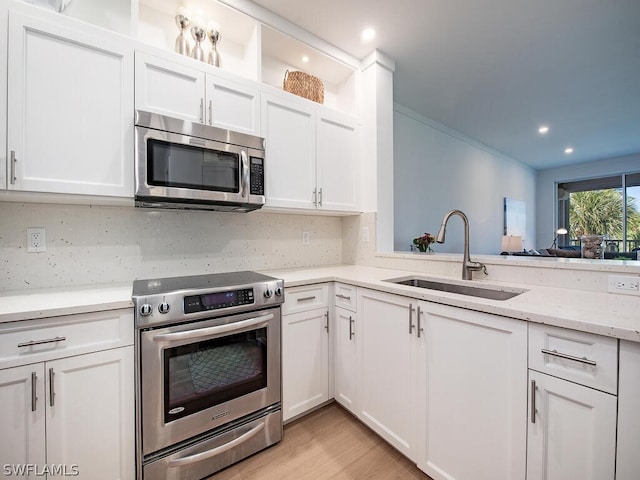 kitchen with light wood-type flooring, tasteful backsplash, stainless steel appliances, sink, and white cabinetry