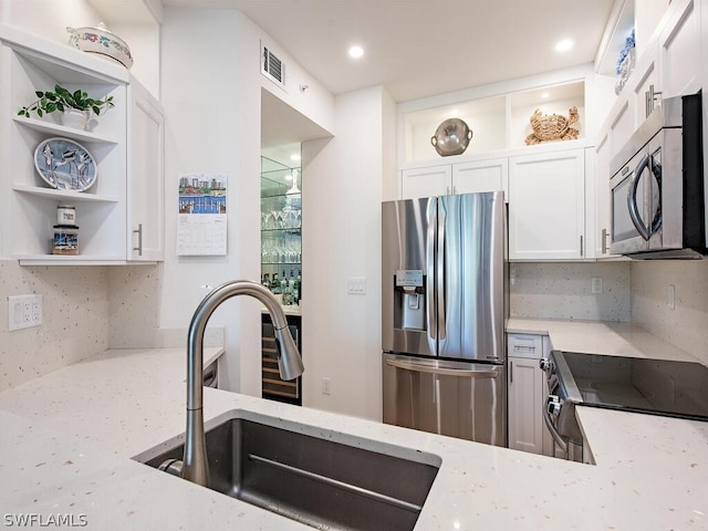 kitchen with decorative backsplash, light stone counters, stainless steel appliances, sink, and white cabinets