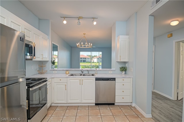 kitchen with a notable chandelier, track lighting, sink, stainless steel appliances, and white cabinets