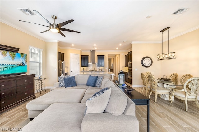 living room with ceiling fan with notable chandelier, light wood-type flooring, and ornamental molding