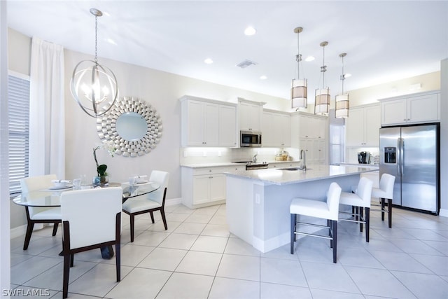 kitchen featuring appliances with stainless steel finishes, hanging light fixtures, tasteful backsplash, an island with sink, and white cabinets