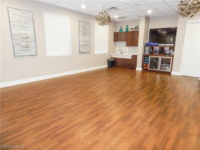 unfurnished living room featuring a drop ceiling, a notable chandelier, and hardwood / wood-style flooring